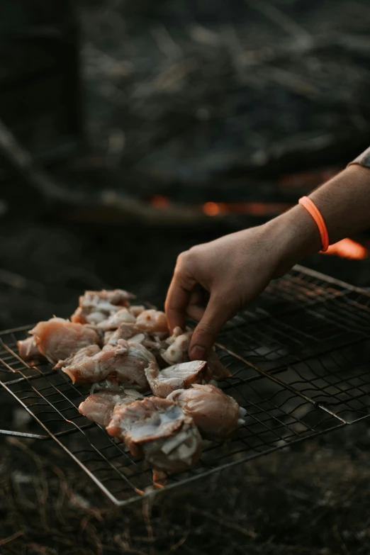 a person with an orange wrist watch reaching for fish on the grill