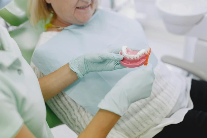 two women with gloves on their hands showing a dental hygiene piece to someone else