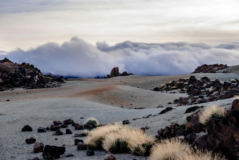 several large rocks, sand and grass with small clouds hanging in the distance