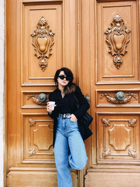 a woman leaning against a door wearing jeans