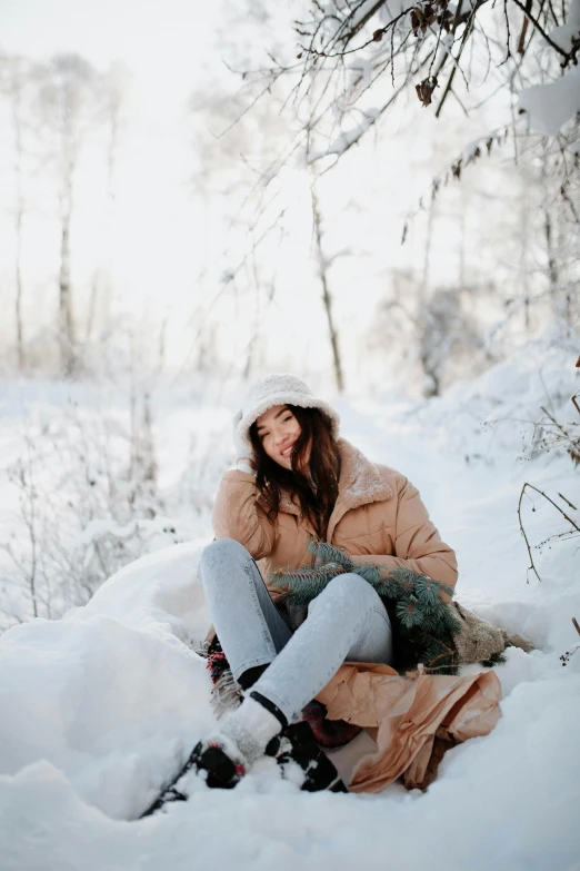 a woman sitting in the snow with a christmas tree on her knees