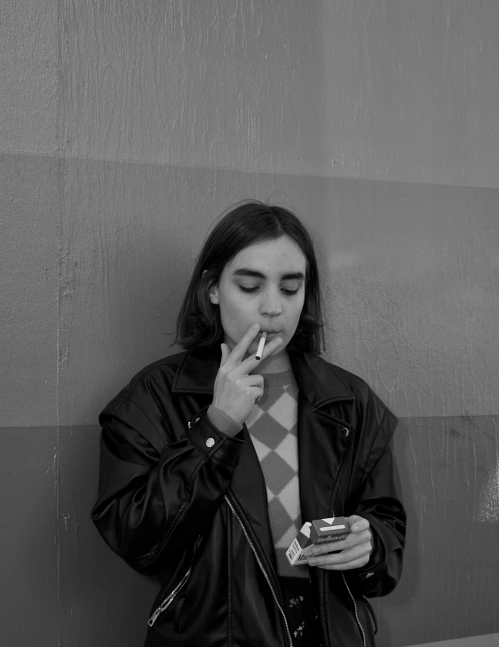 a woman is smoking a cigarette near a wall