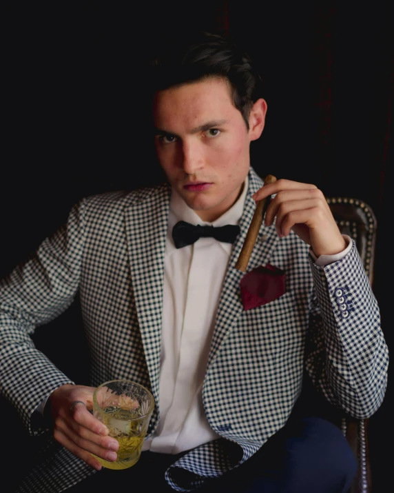 a man in a tuxedo and bow tie holds a drink