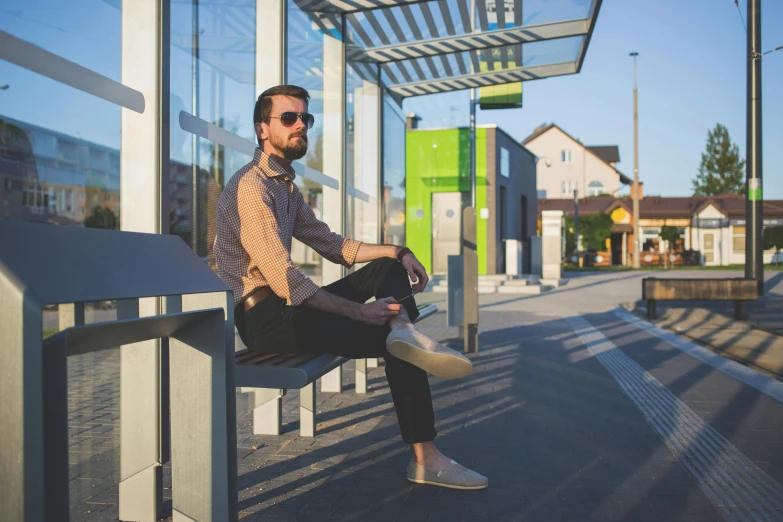 man with sunglasses on sitting at city bus stop