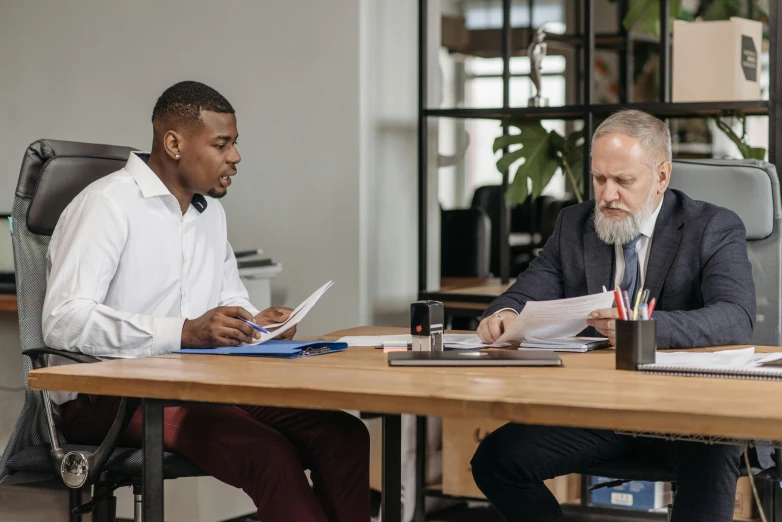 two men sitting at a table with papers and pens