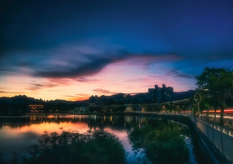 night falls on the city skyline, with street lights reflected in a pond