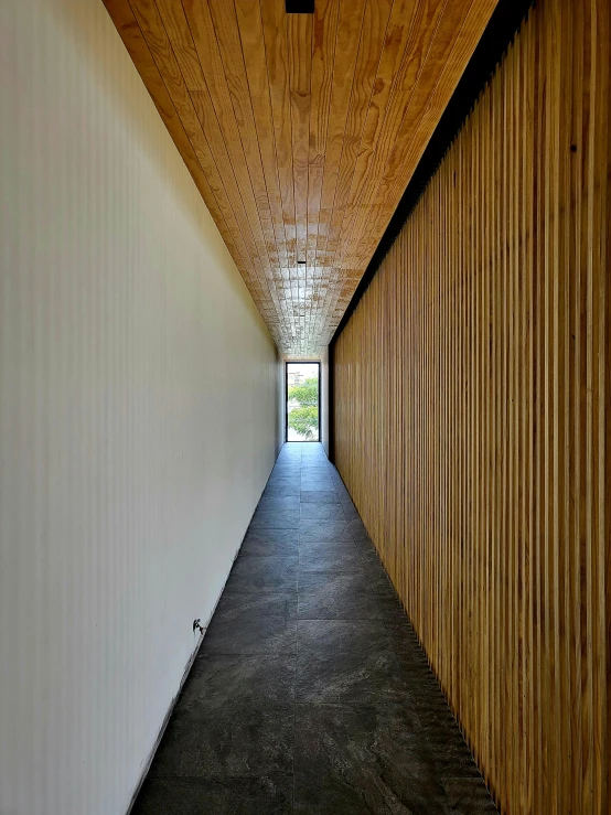 a long corridor with several walls, wooden slats on the ceiling and metal accents to one side