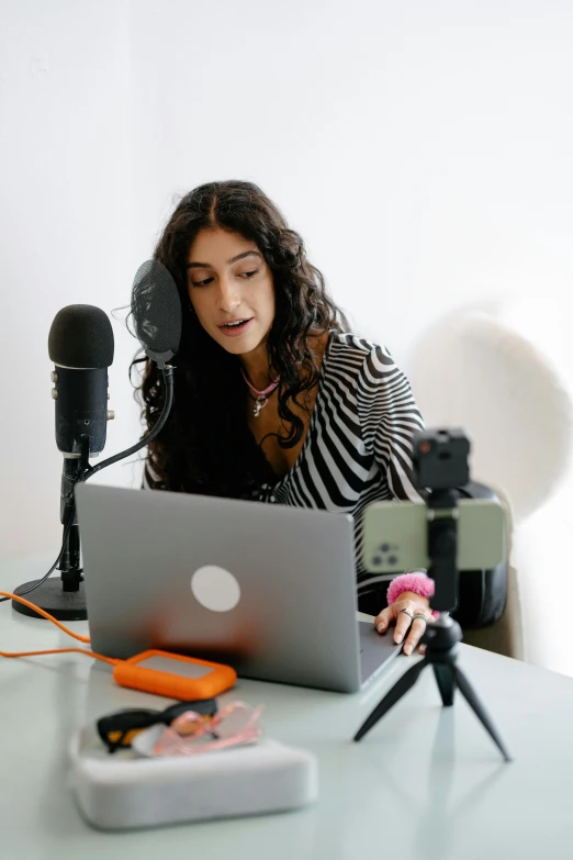 a woman sitting at a desk on her laptop and recording music