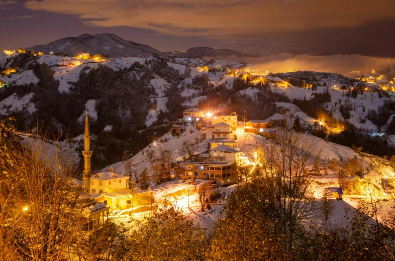 the view of a town at night, with a snowy mountain behind it