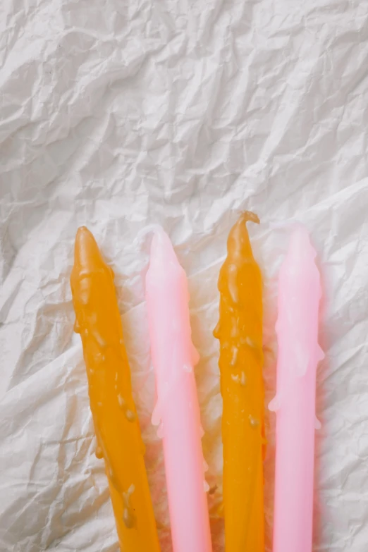 two candles are laying on some paper with pink frosting