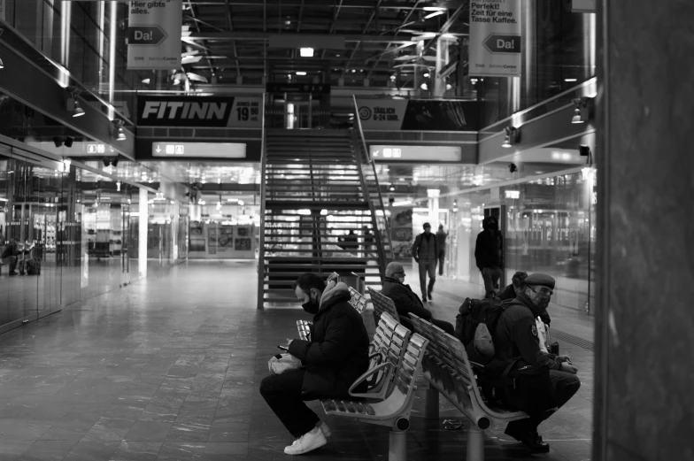 some people are sitting on benches in an empty building