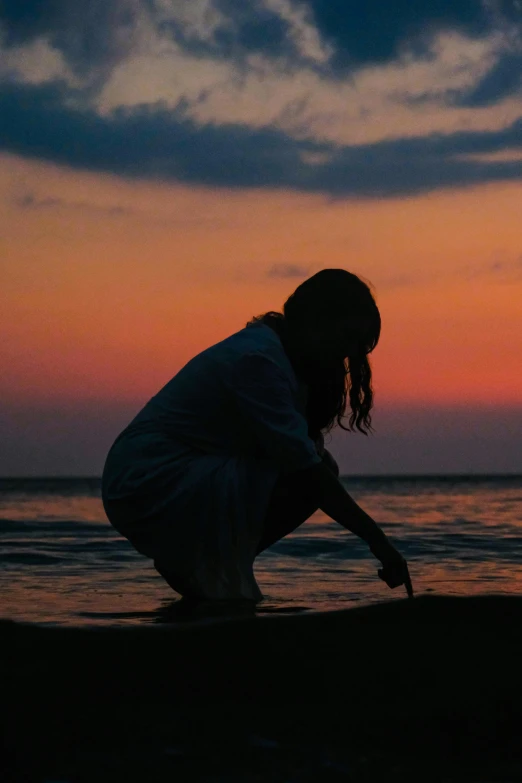 the woman is kneeling on the beach while watching the sun go down