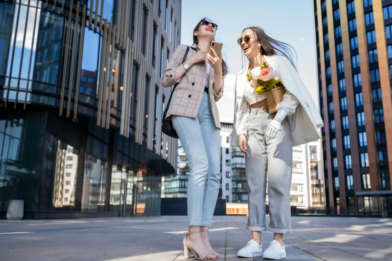 two women posing on a city street and one is holding flowers