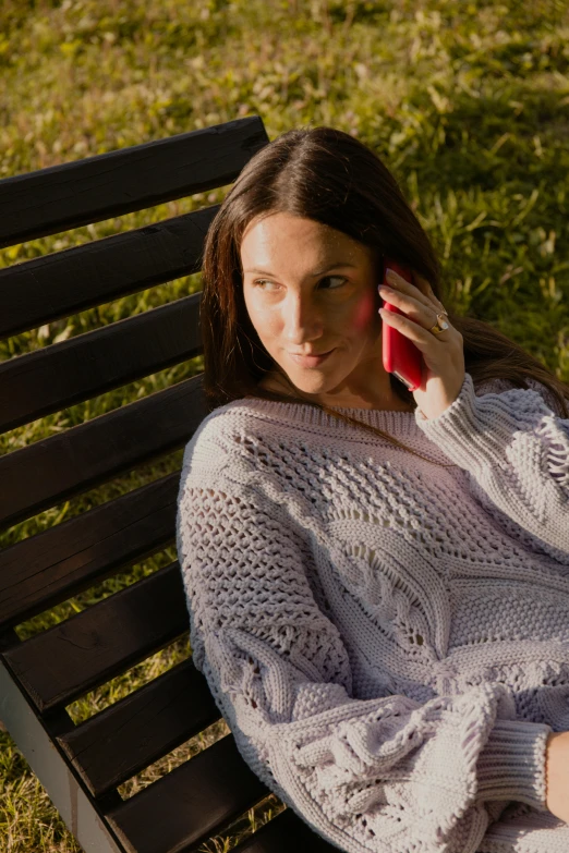 a woman is sitting on a bench talking on a red cell phone