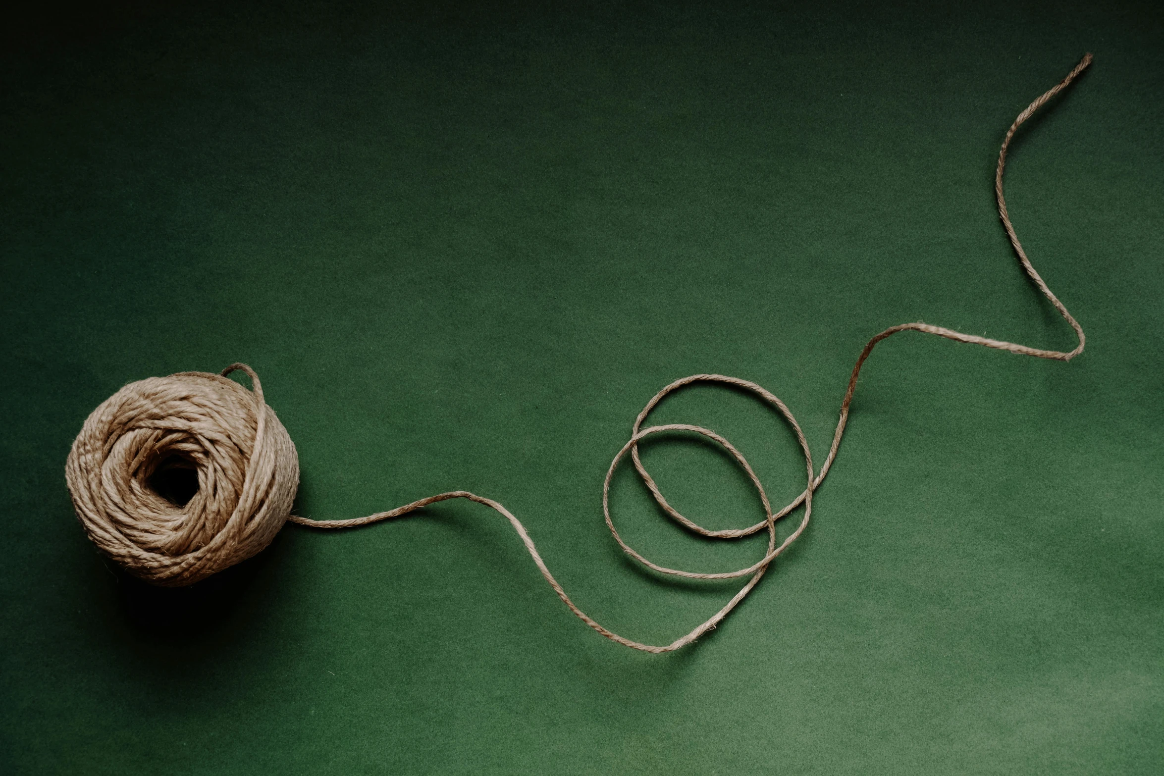 a string rope sits on the floor and next to a ball of yarn