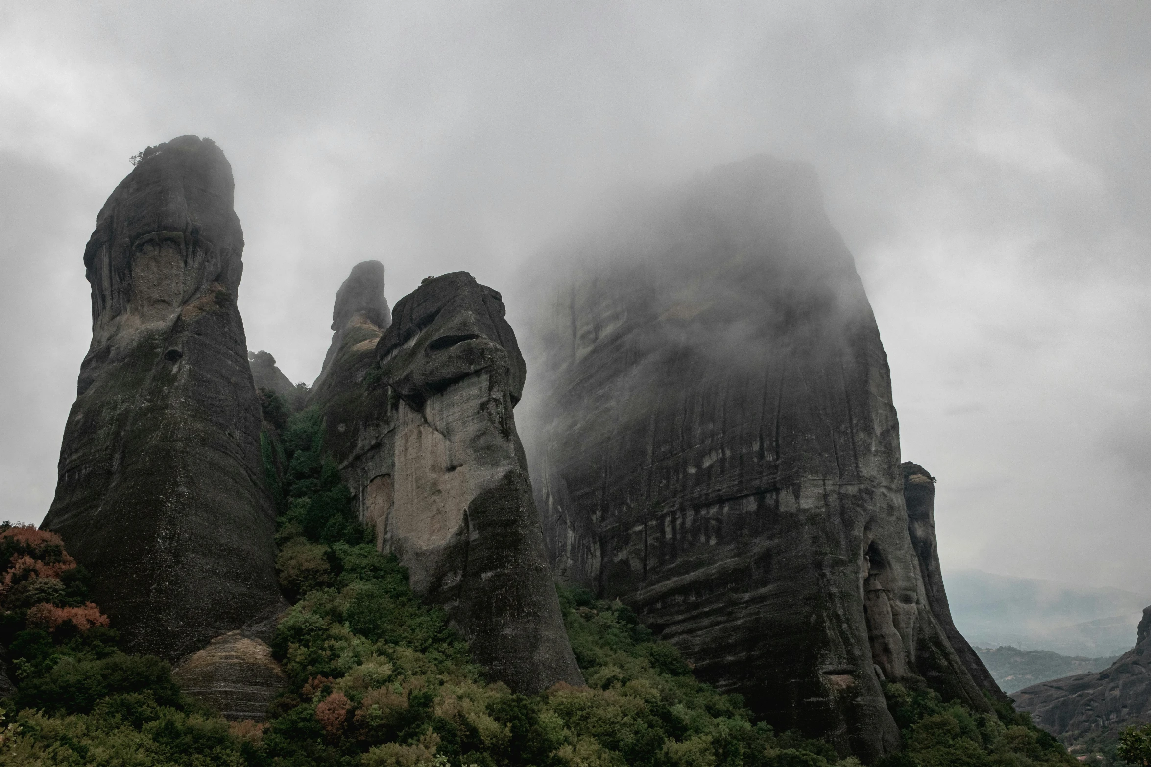 fog rolls over a rock formation, with tall mountains in the background