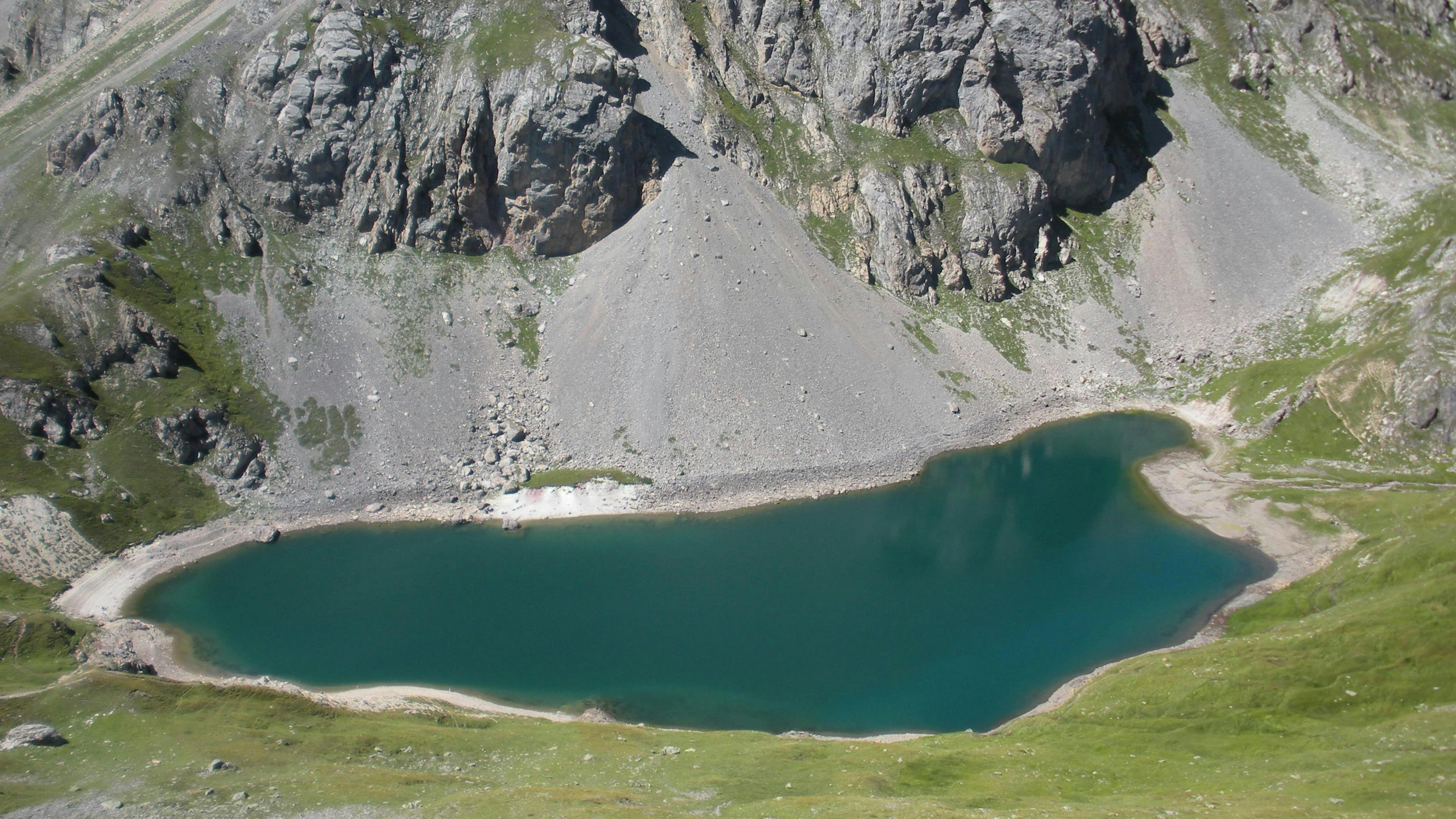 an aerial view of a green lake surrounded by rocky mountains