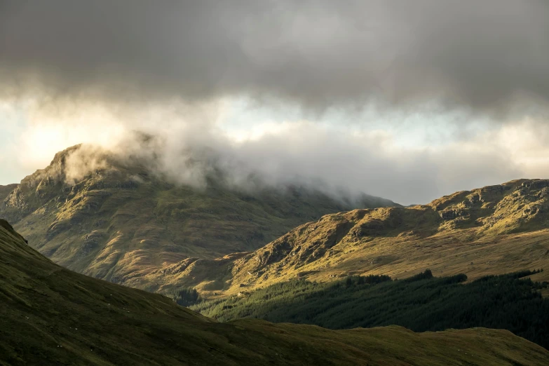 a grassy hill under storm clouds and sunlight