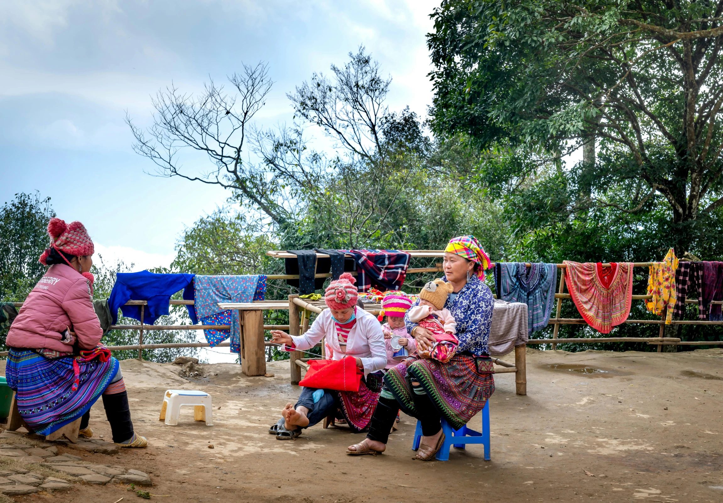 three women sit outside on a bench by their laundry line