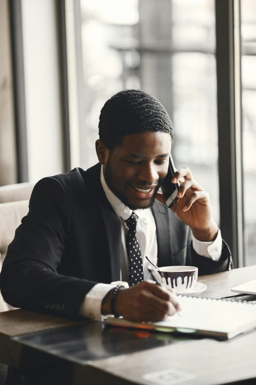 a man in a business suit sitting at a table with a notepad and coffee