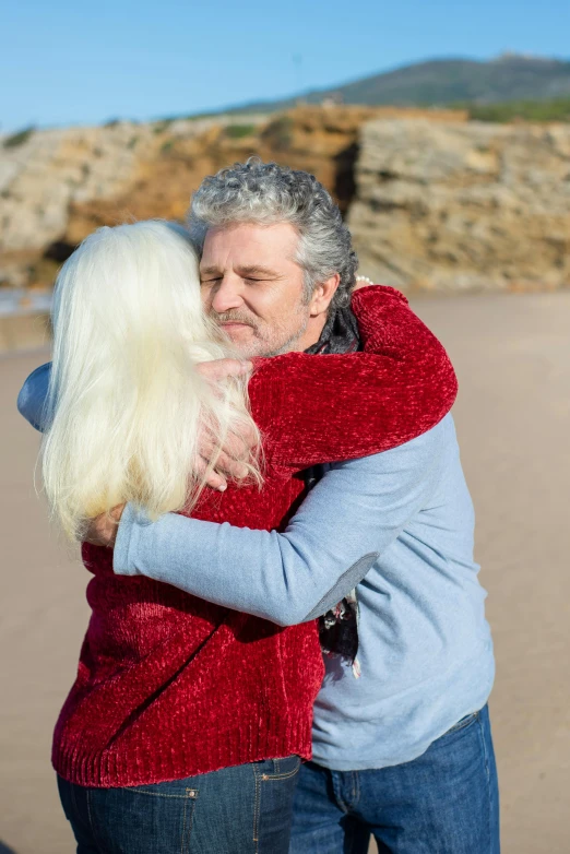 a man hugs his long white hair on the beach