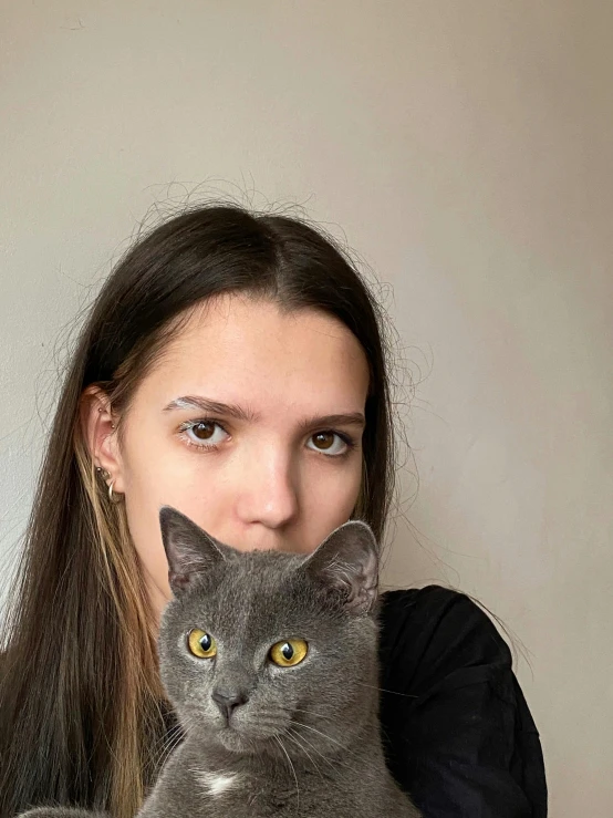 woman with long hair holding gray cat in front of face