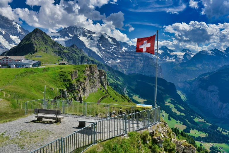 a swiss flag flying over the mountains above a city