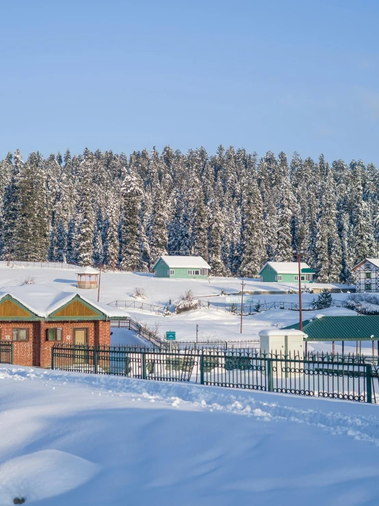 a snowy town with wooden buildings, a red fence and lots of trees