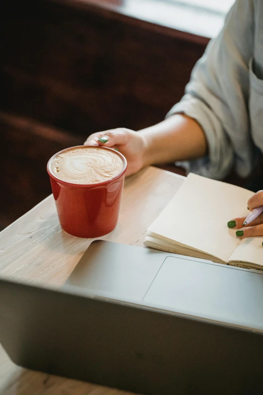 person holding a cup of coffee while sitting at a wooden table