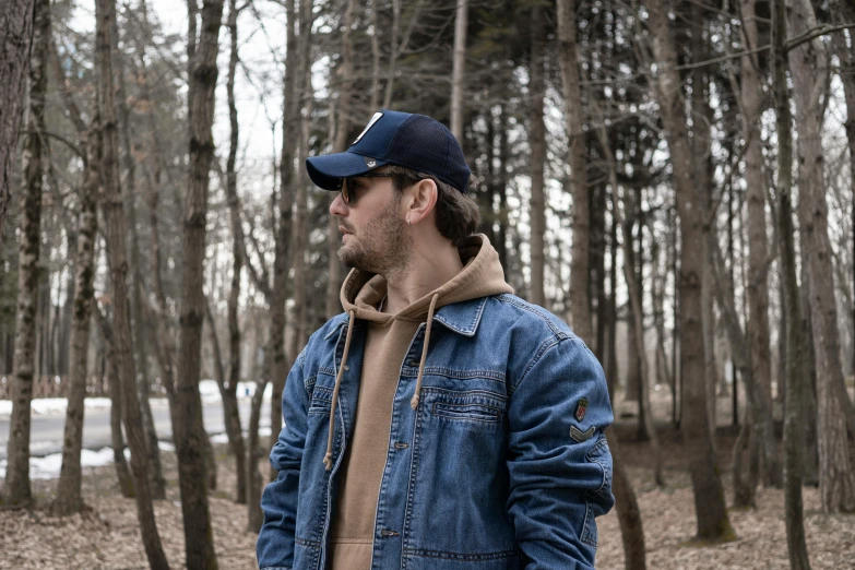 a man in a blue denim jacket is looking in the woods