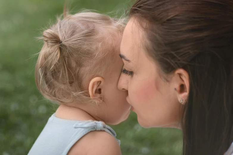 a young woman kissing her baby who is wearing silver ear pins