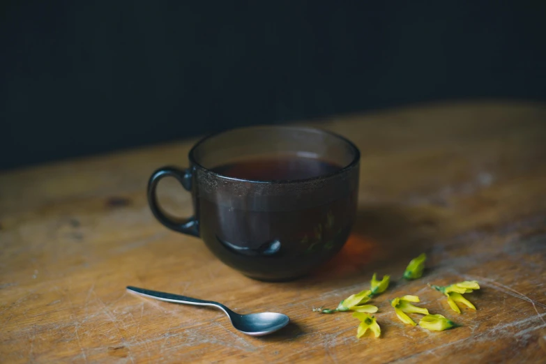 there is a cup of tea next to a spoon and flower buds