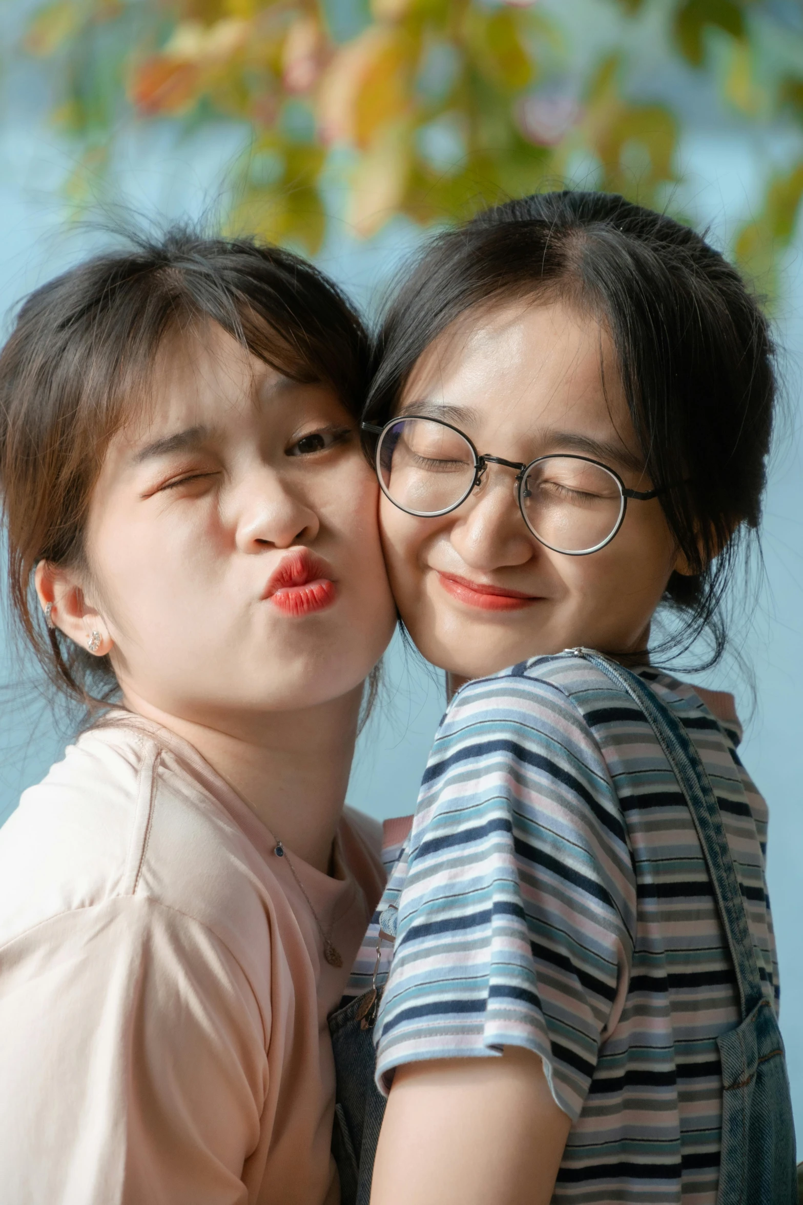 two young children wearing glasses kiss in front of a tree