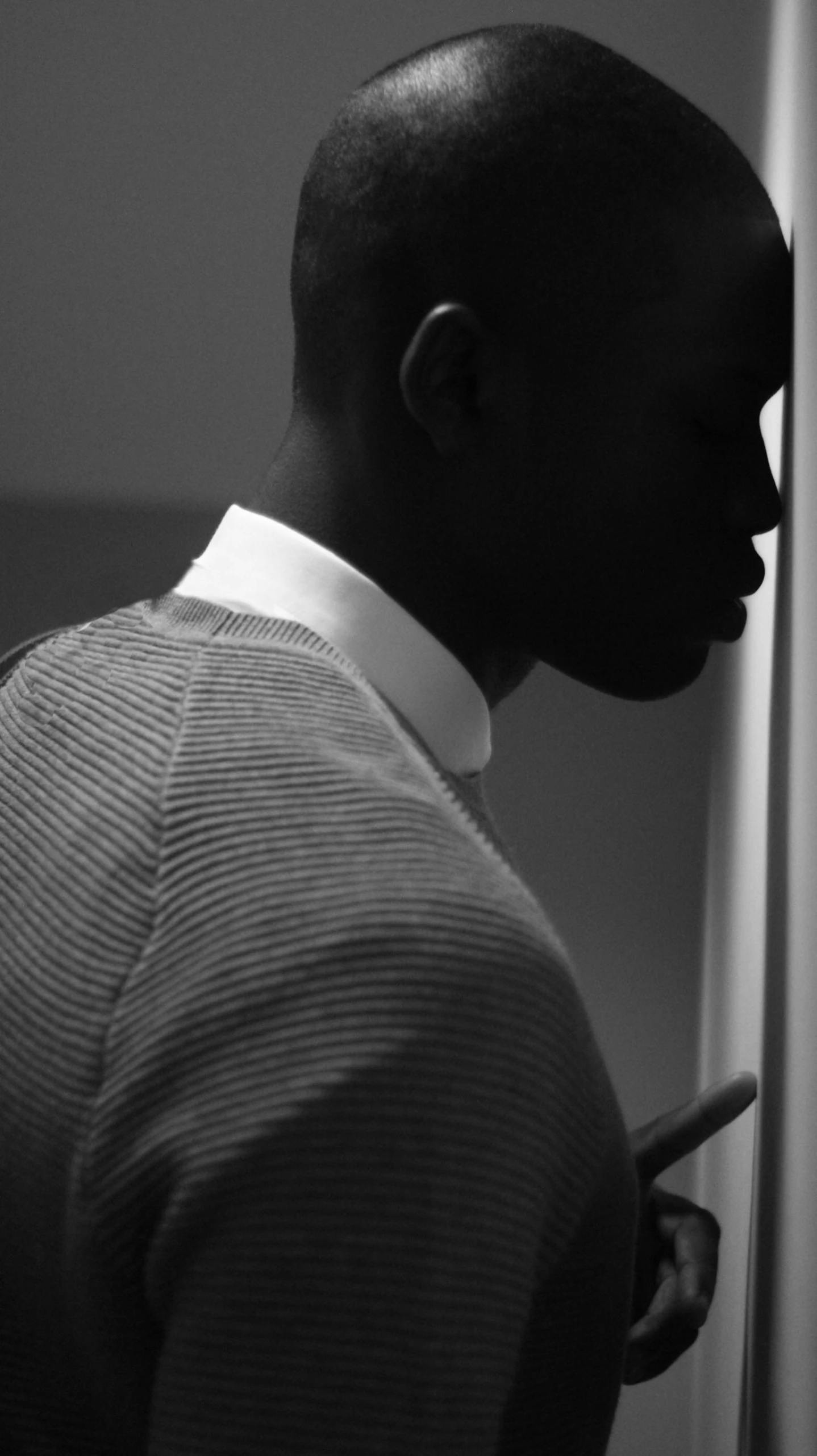 a man in a suit, tie and collar stands with his hand on a wall