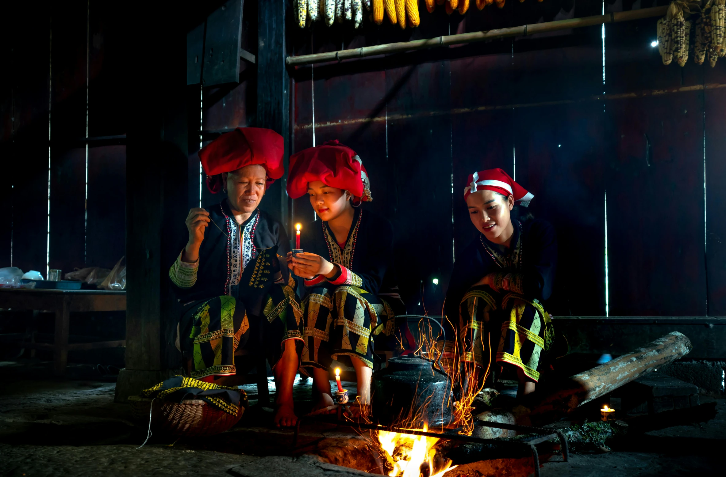 the asian people dressed in the traditional dress and wearing headwear stand near an open fire