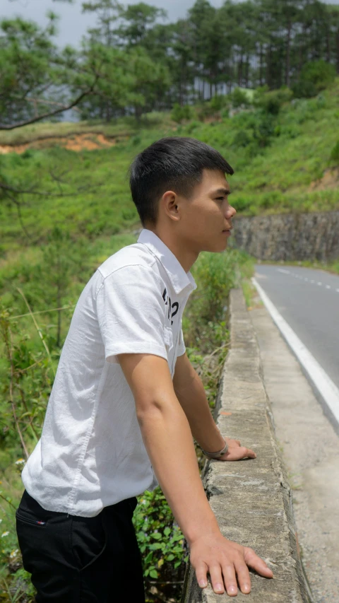 a man leaning on the side of a long brick wall next to a street