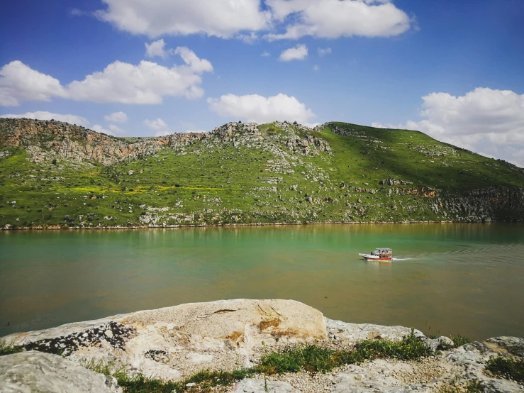 a boat sailing down the water next to a rocky shore