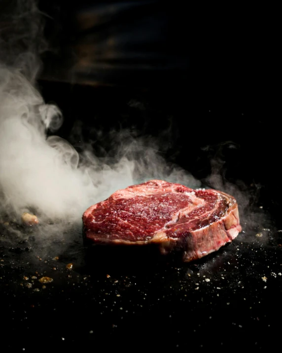 raw beef sitting on a surface being cooked by the smoke from the burner
