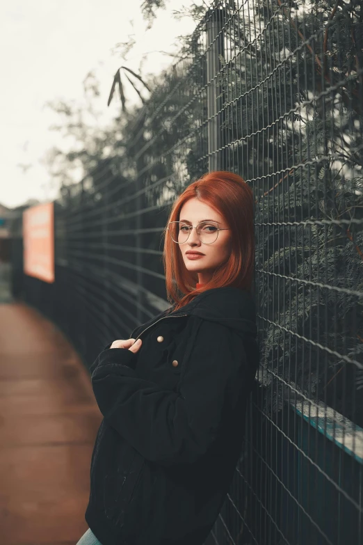 a beautiful redhead woman standing against a fence