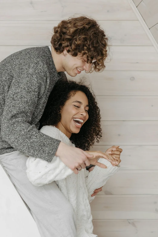 a couple smiles while sitting together under a white and wooden wall