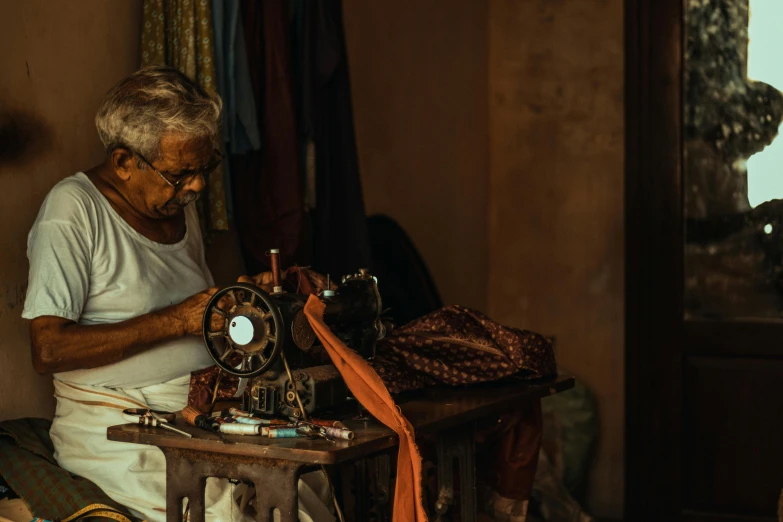 an old man sews a piece of cloth with a vintage sewing machine