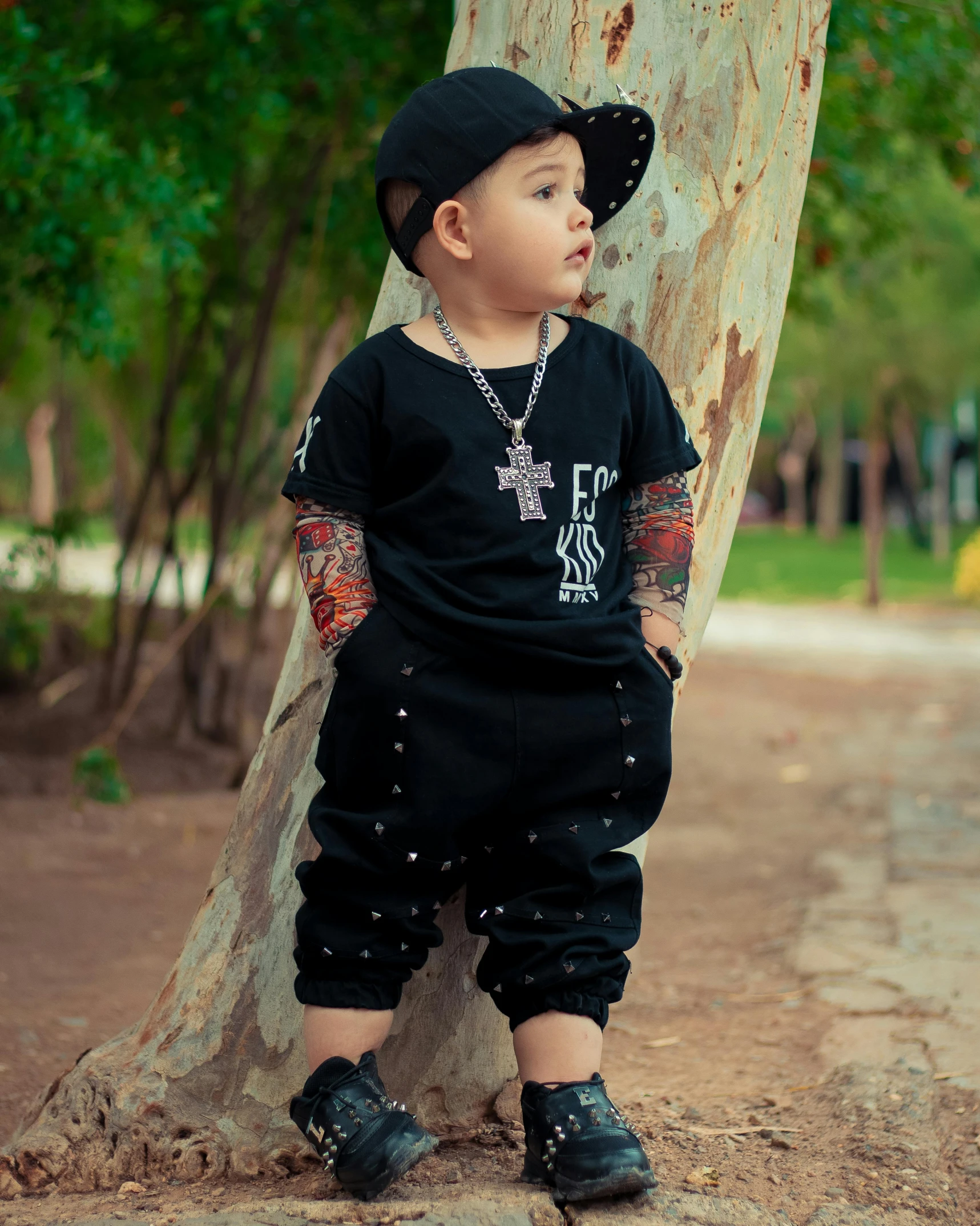 small  in black outfit standing by a tree