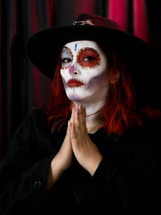 the woman wearing her face painted red has a black hat and her hand over her face