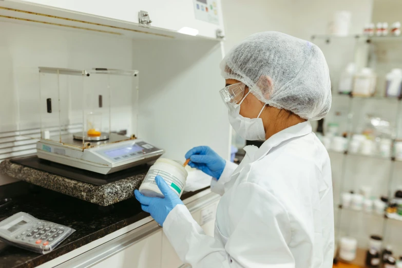 a woman in white coat and gloves pouring soing into jar