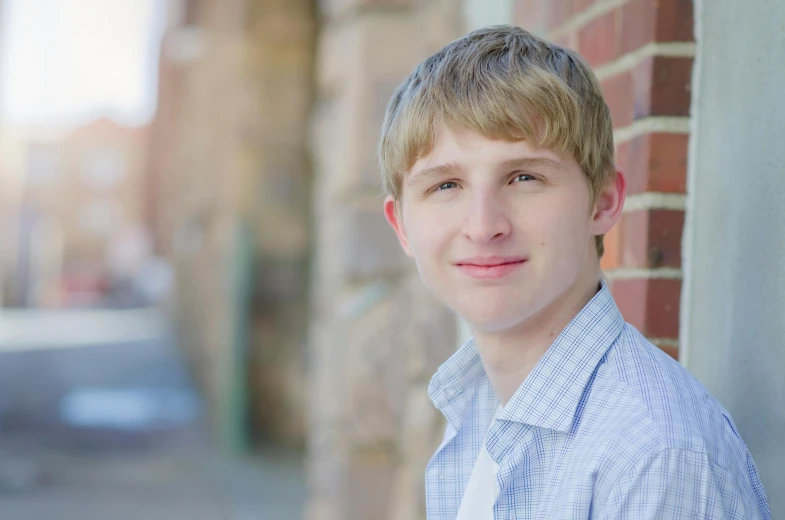 a boy in a on - up is standing by a brick wall