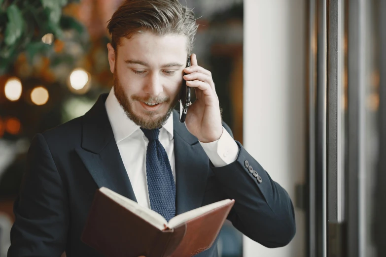 a man in business clothes holding a book while talking on a phone