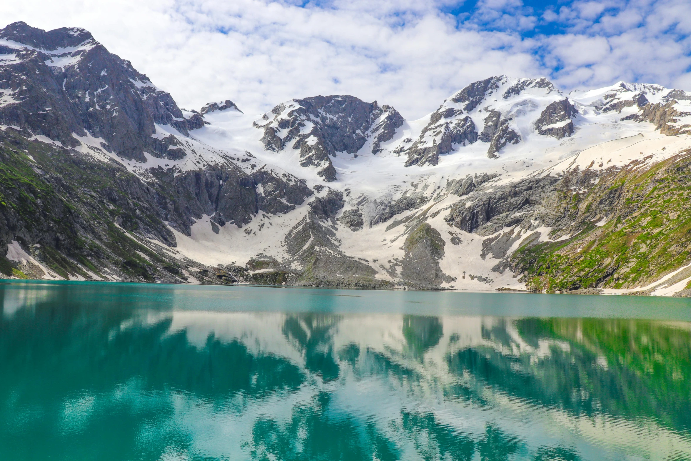 a lake surrounded by snowy mountains and clouds