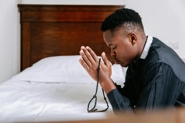 young man praying on a bed with his hands on his chest