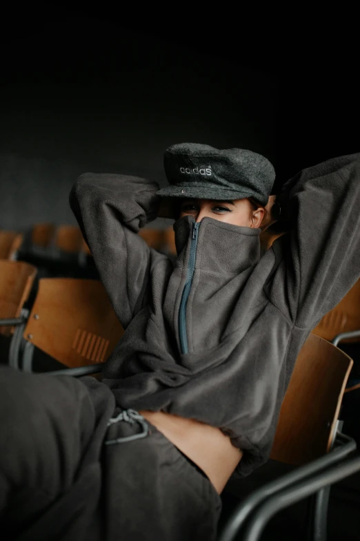 a woman is wearing a hood and sitting in an empty chair