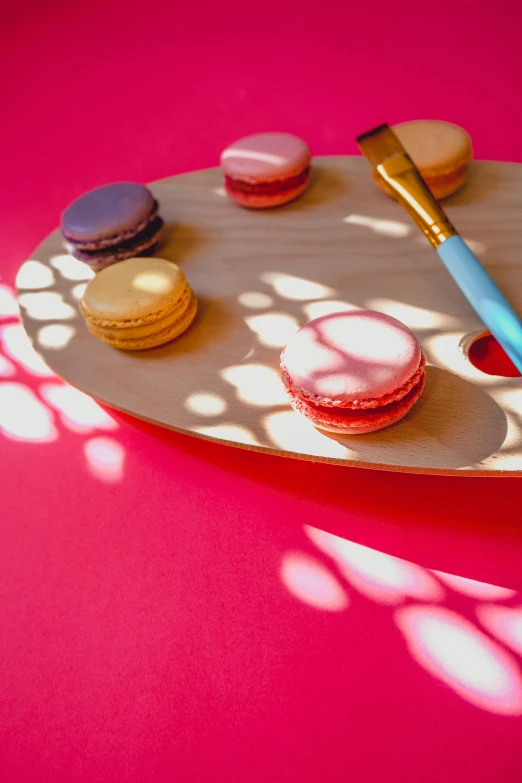 a wood plate topped with macaroons on a pink table